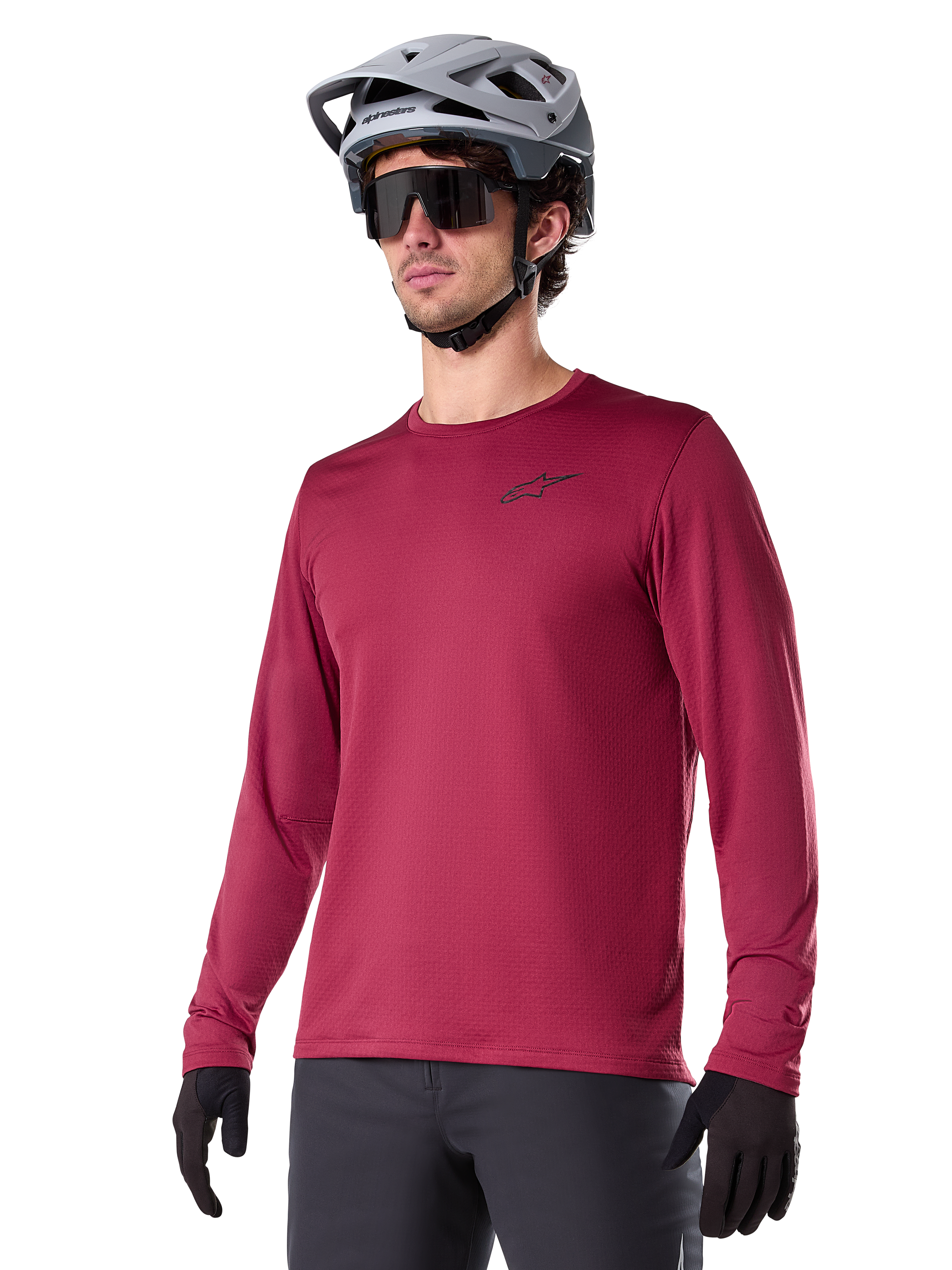 Alpinestars A-Dura Thermal Jersey, koszulka rowerowa MTB z długim rękawem, bordowa, z izolującą podszewką z polaru i małym czarnym logo na klatce piersiowej, noszona z szarym kaskiem, czarnymi okularami przeciwsłonecznymi i czarnymi rękawiczkami, zaprojektowana do jazdy w chłodne dni