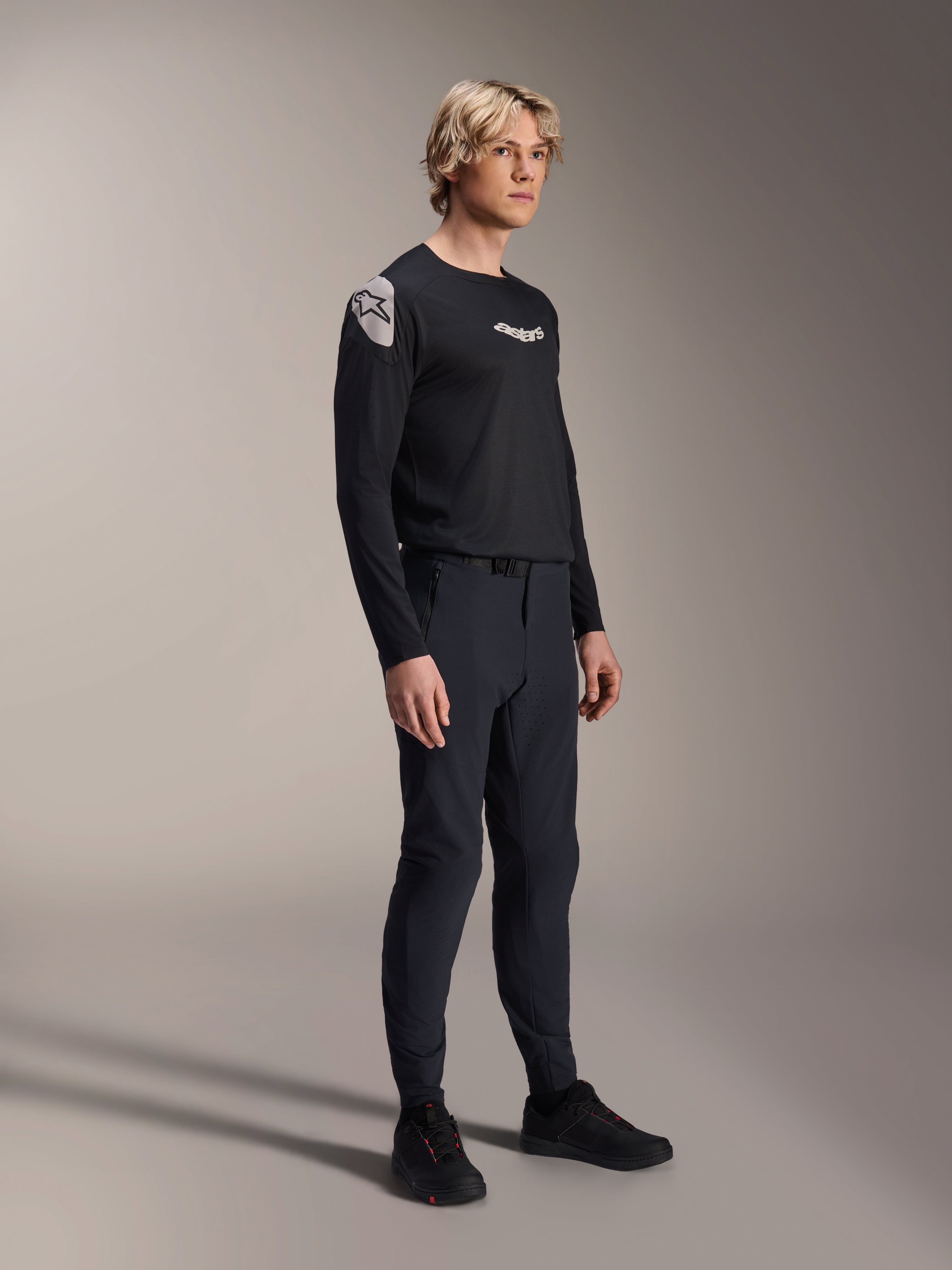 Męski model w spodniach Alpinestars A-Aria Elite w kolorze Black Titanium i koszulce Aria Polartec Elite LS, czarny wyczynowy strój do kolarstwa górskiego, laserowa perforacja i magnetyczne zapięcie klamry w spodniach, koszulka z długim rękawem z białymi logotypami, kompletny strój do jazdy terenowej