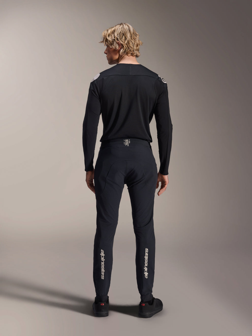Alpinestars A-Aria Polartec Elite Long Sleeve Jersey, czarna koszulka MTB, widok z tyłu w zestawie z dopasowanymi czarnymi spodniami, sportowy krój do kolarstwa górskiego, techniczny materiał odprowadzający wilgoć, subtelne logo w dolnej części pleców