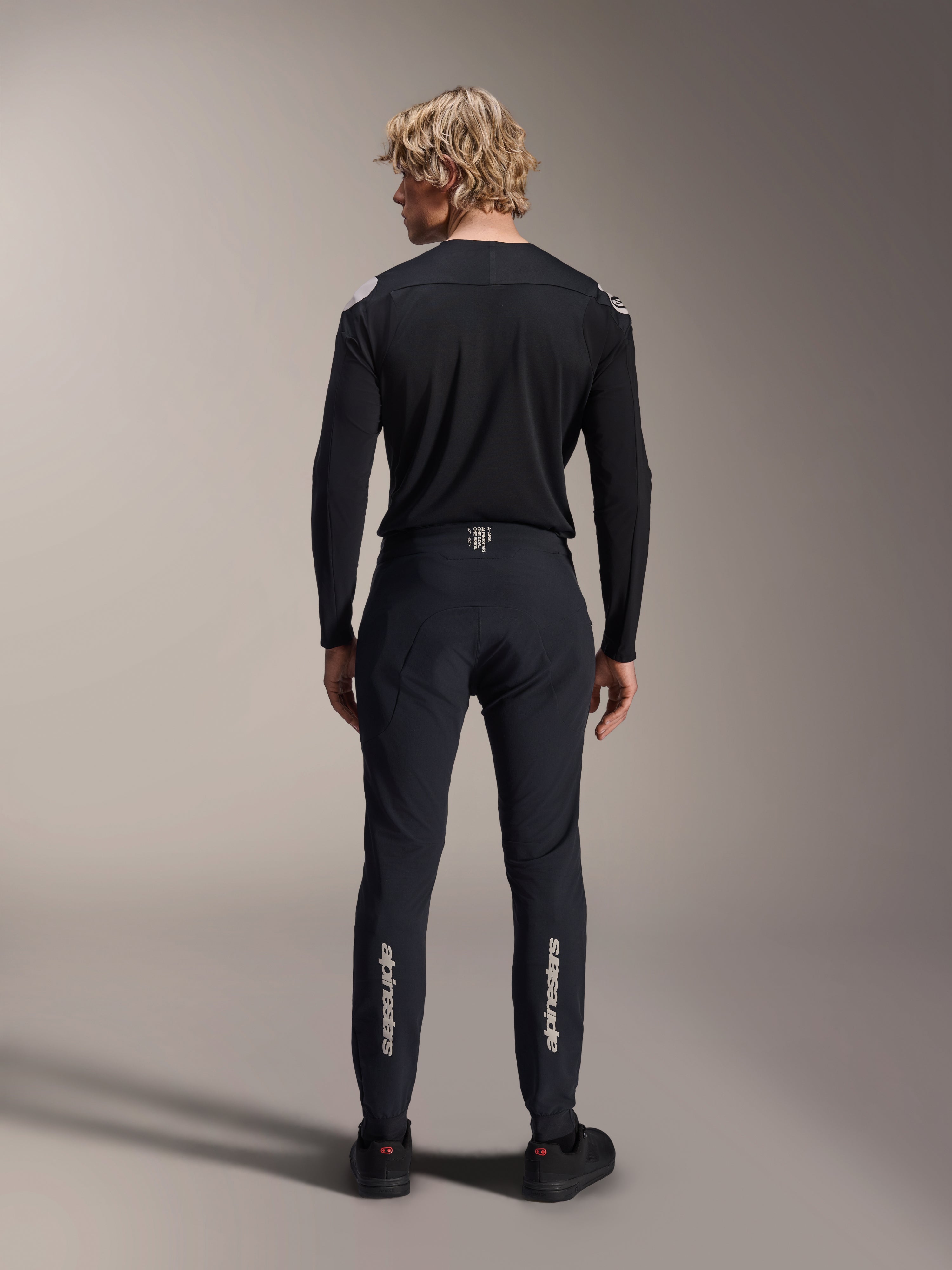 Alpinestars A-Aria Polartec Elite Long Sleeve Jersey, czarna koszulka MTB, widok z tyłu w zestawie z dopasowanymi czarnymi spodniami, sportowy krój do kolarstwa górskiego, techniczny materiał odprowadzający wilgoć, subtelne logo w dolnej części pleców