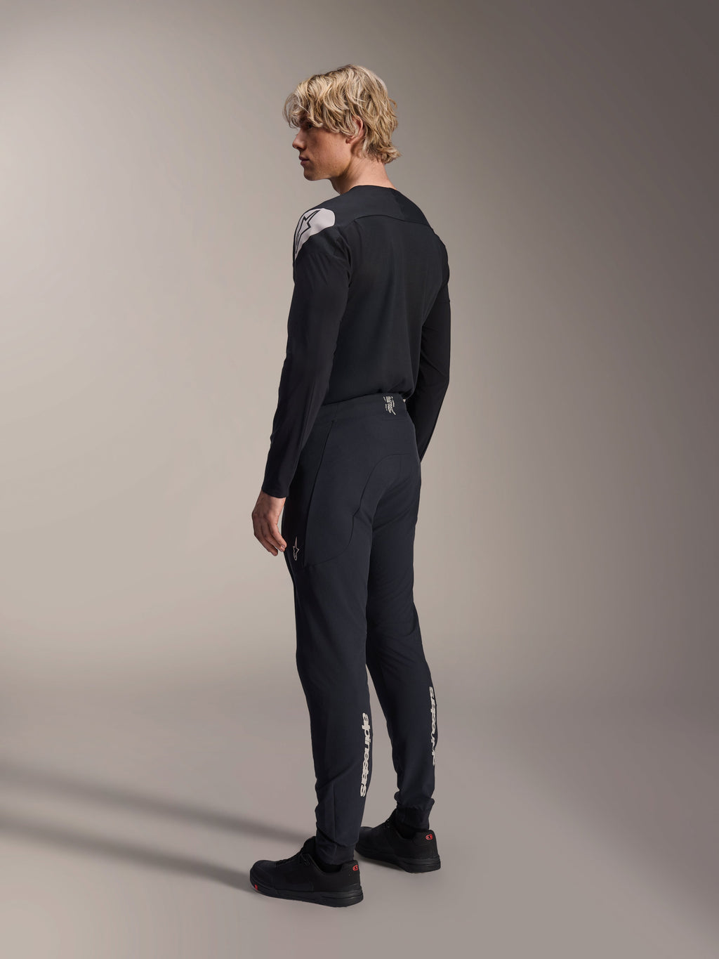 Alpinestars A-Aria Polartec Elite Jersey - Long Sleeve, czarna, prezentowana przez modela z profilu od tyłu, białe logo na ramieniu, w zestawie z pasującymi czarnymi spodniami rowerowymi, profesjonalny strój MTB