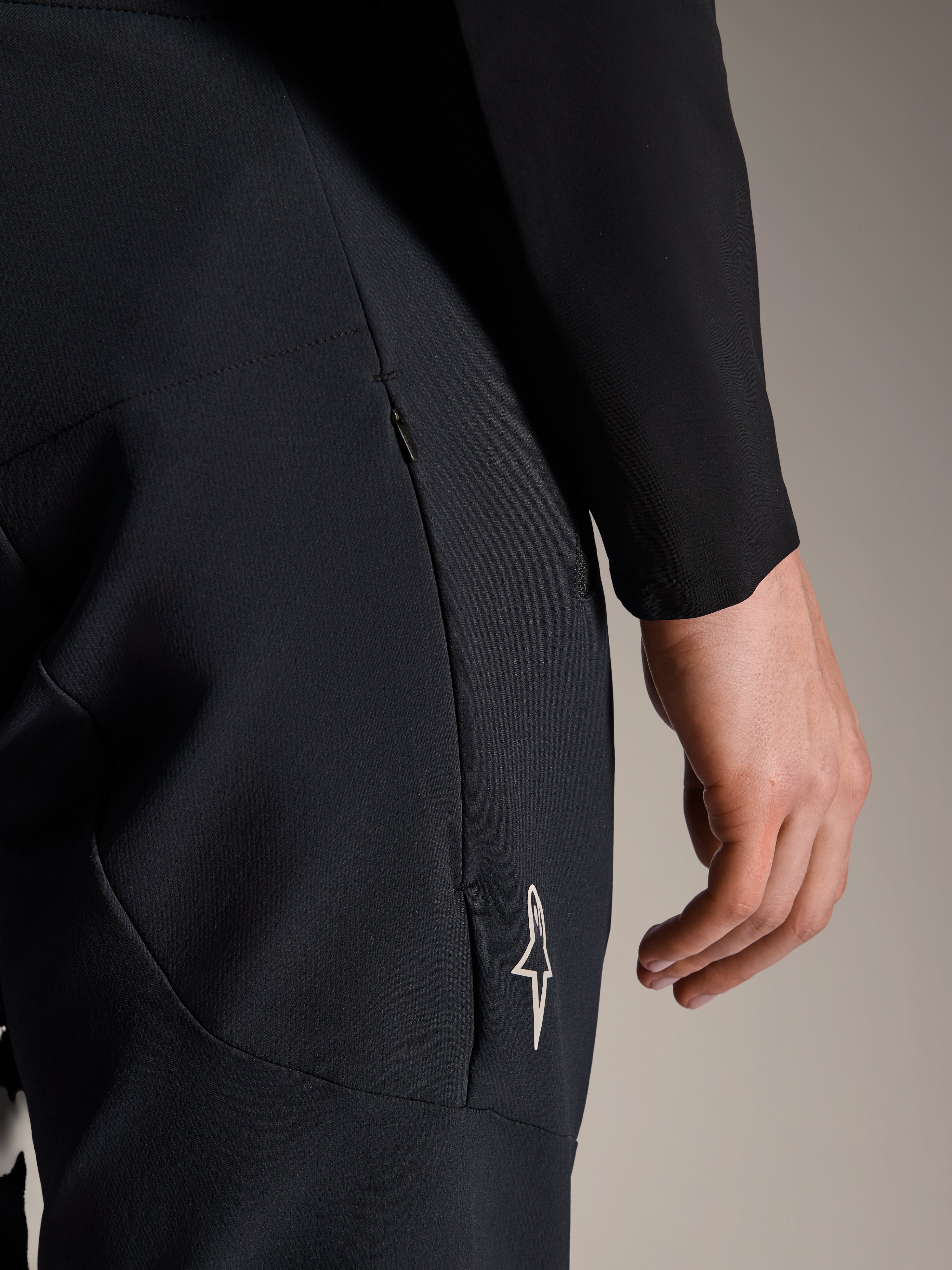 Alpinestars A-Aria Elite Pants w kolorze Black Titanium, zbliżenie na boczną kieszeń zapinaną na zamek i małe białe logo gwiazdy, techniczne spodnie rowerowe MTB zaprojektowane z myślą o wydajności