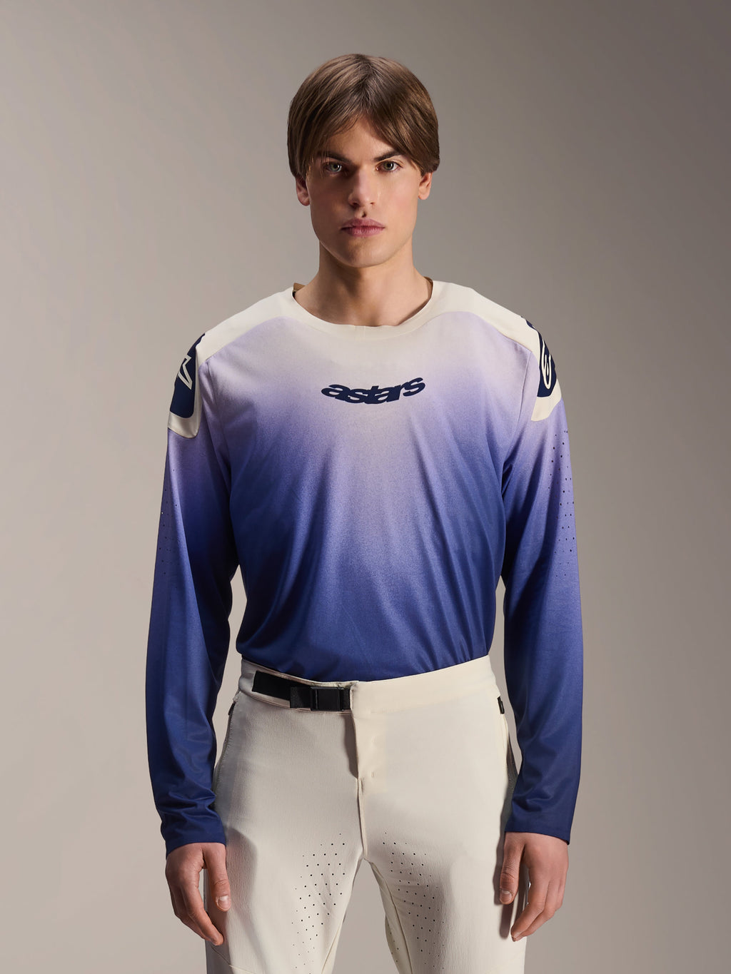 Alpinestars A-Aria Polartec Maker Elite Jersey, koszulka MTB z długim rękawem, kolor Baja Blue z gradientem od bieli do niebieskiego, noszona przez modela w białych spodniach, z ciemnoniebieskim logo na klatce piersiowej i laserowymi perforacjami na rękawach, wyczynowa odzież do kolarstwa górskiego