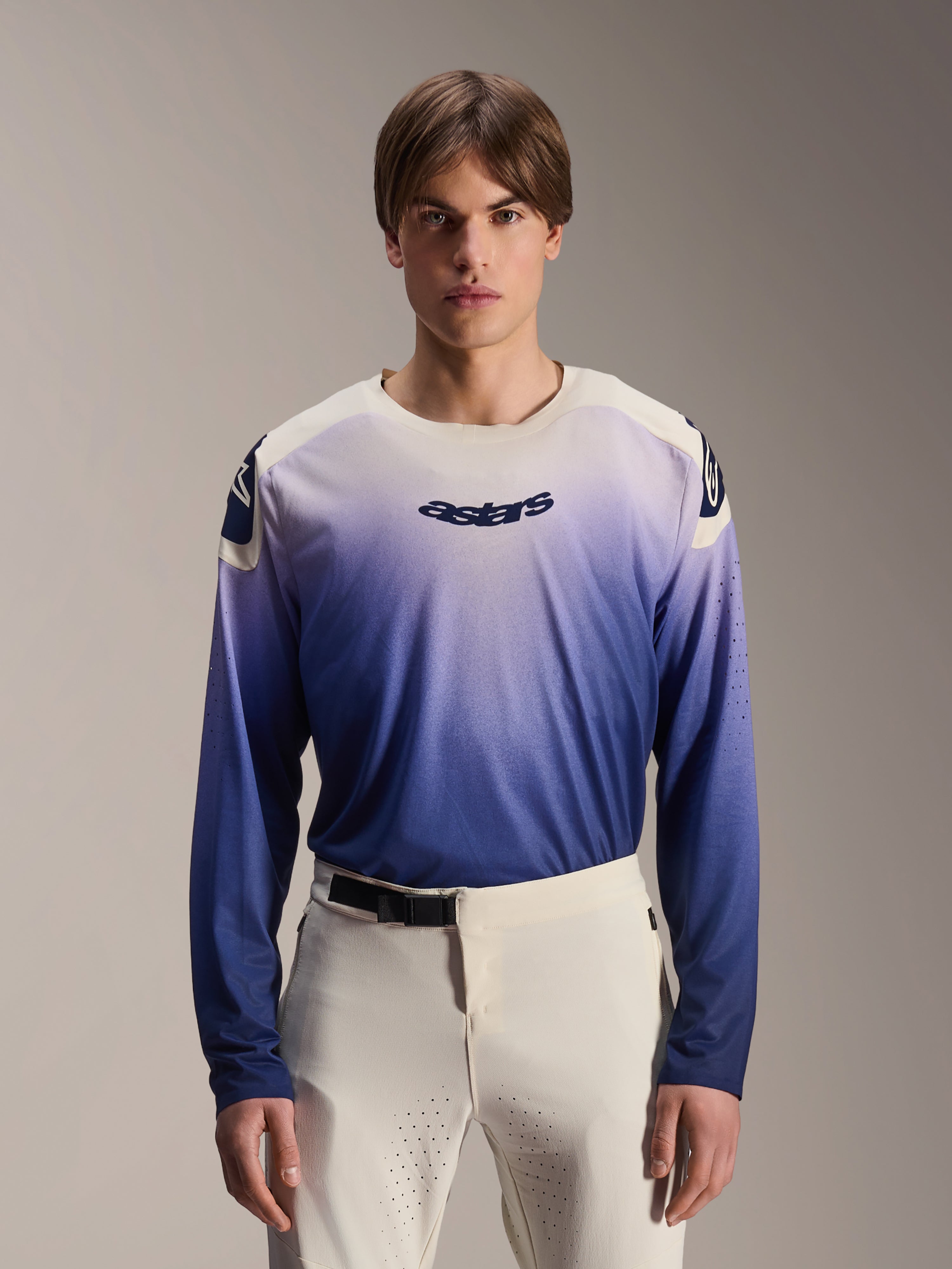 Alpinestars A-Aria Polartec Maker Elite Jersey, koszulka MTB z długim rękawem, kolor Baja Blue z gradientem od bieli do niebieskiego, noszona przez modela w białych spodniach, z ciemnoniebieskim logo na klatce piersiowej i laserowymi perforacjami na rękawach, wyczynowa odzież do kolarstwa górskiego