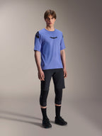 Male model wearing Alpinestars A-Aria Polartec Elite Short Sleeve Jersey in Baja Blue, paired with black MTB shorts and knee guards, featuring black Astars logos on the chest and shoulder, premium performance mountain bike gear