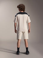 Alpinestars A-Aria Polartec Elite Short Sleeve Jersey, rowerowa koszulka MTB, kolor ecru z czarnymi panelami na ramionach, widok z tyłu z pasującymi szortami i czarnymi skarpetami, krój performance z wydłużonym tyłem do jazdy w terenie