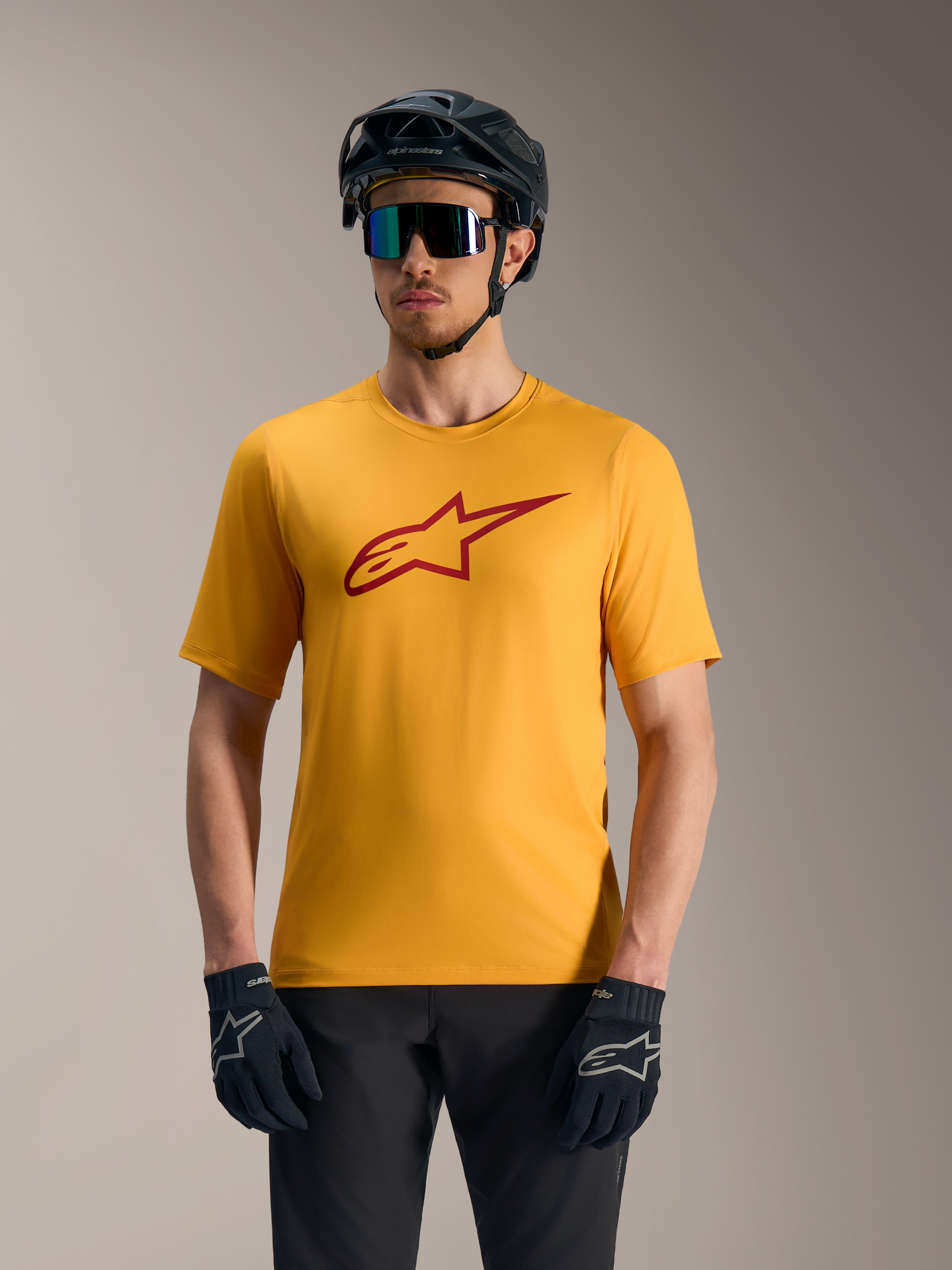 Pomarańczowa koszulka A-Dura Ride z krótkim rękawem, czerwone logo Astars, kask MTB i rękawiczki rowerowe.