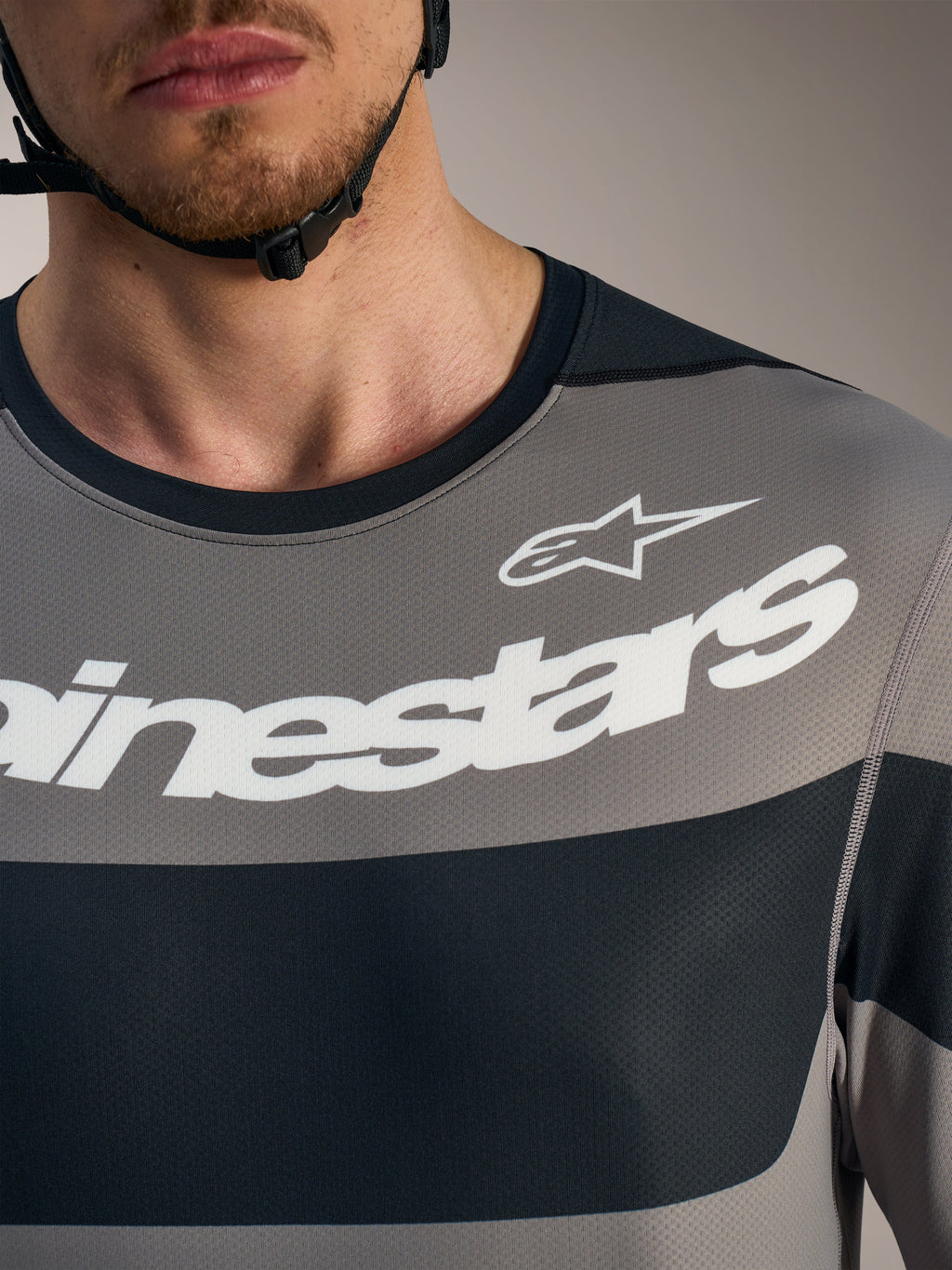 Szara koszulka Alpinestars A-Dura Race, detal klatki piersiowej z białym logo i techniczną siateczką.
