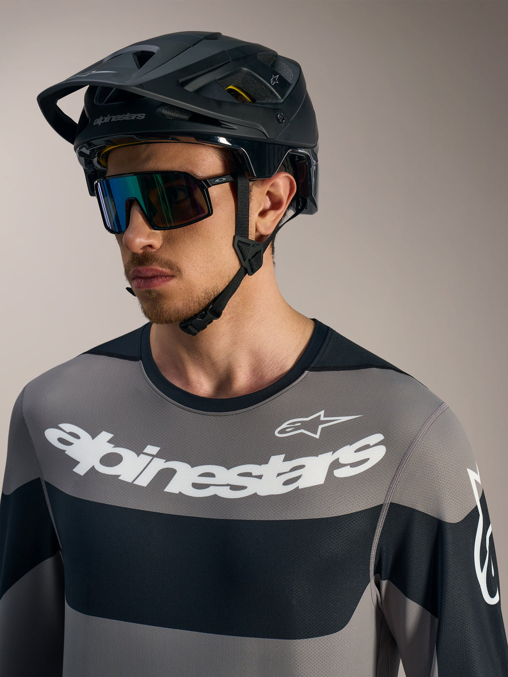 Alpinestars A-Dura Race LS, szara koszulka z białym logo, czarny kask MTB i okulary przeciwsłoneczne.