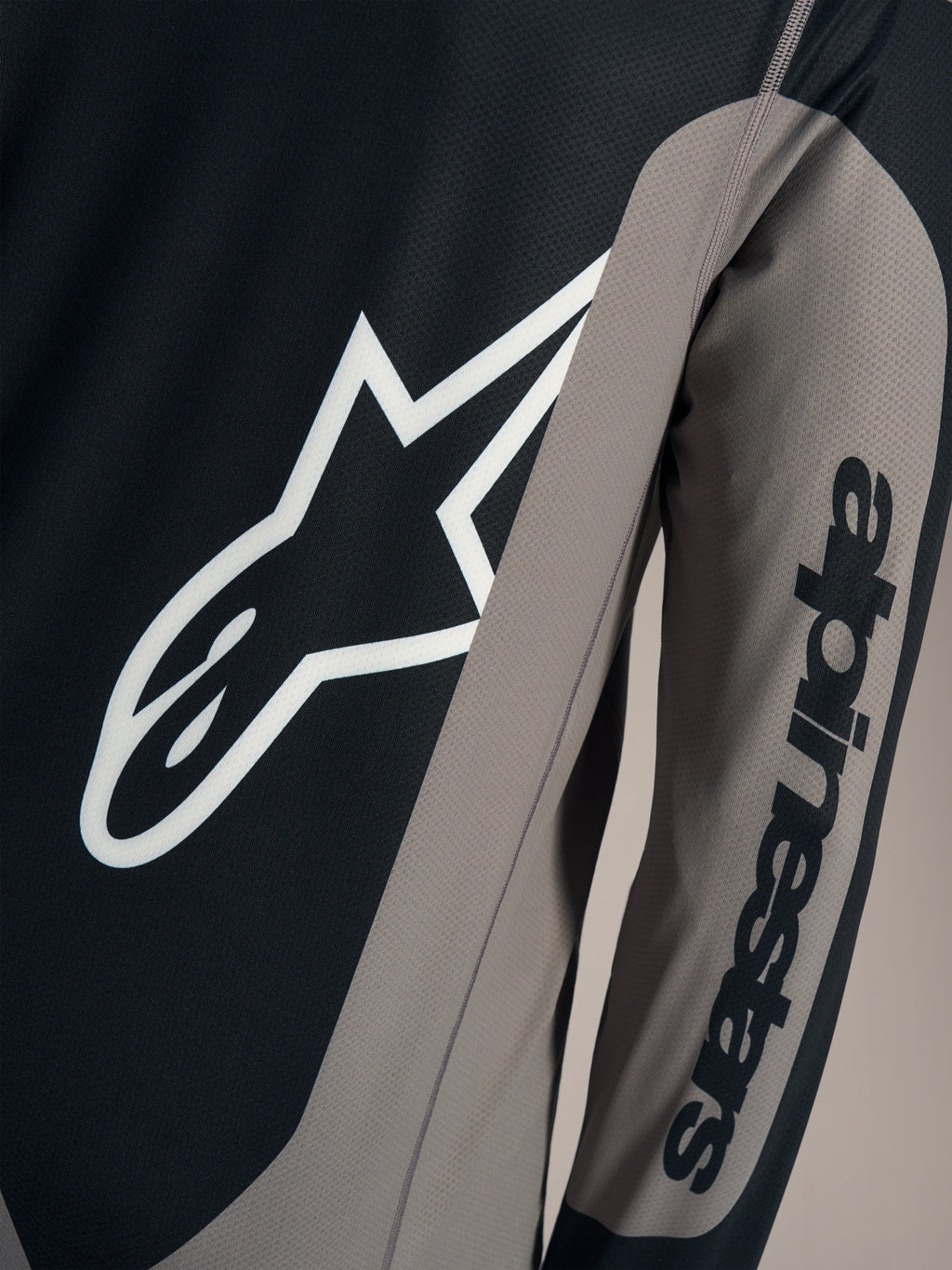 Szara koszulka A-Dura Race z długim rękawem, białe logo Astars na piersi i napis Alpinestars na rękawie.