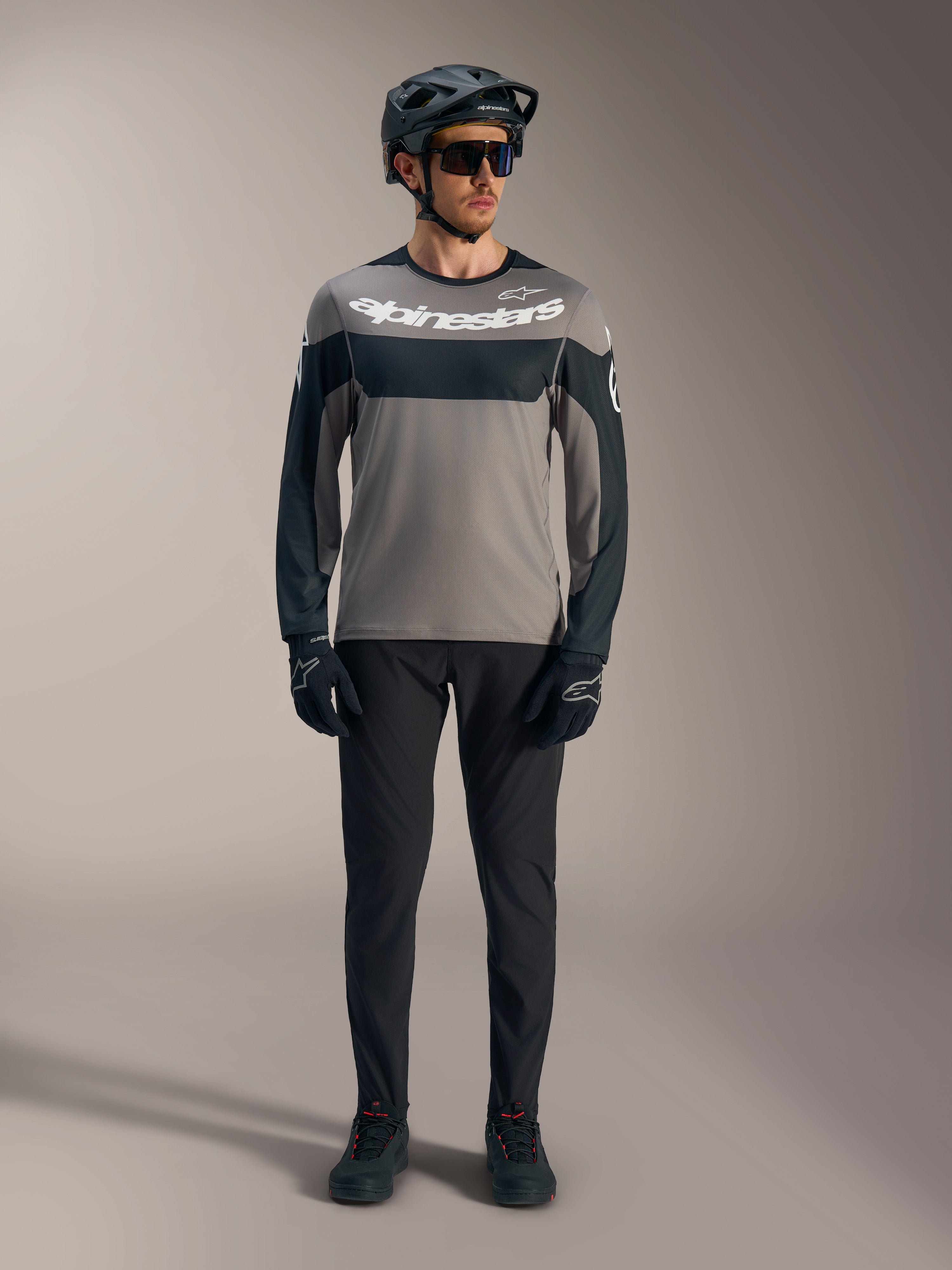 Szaro-czarna koszulka A-Dura Race z długim rękawem i białym logo Alpinestars, zestawiona ze sprzętem MTB.