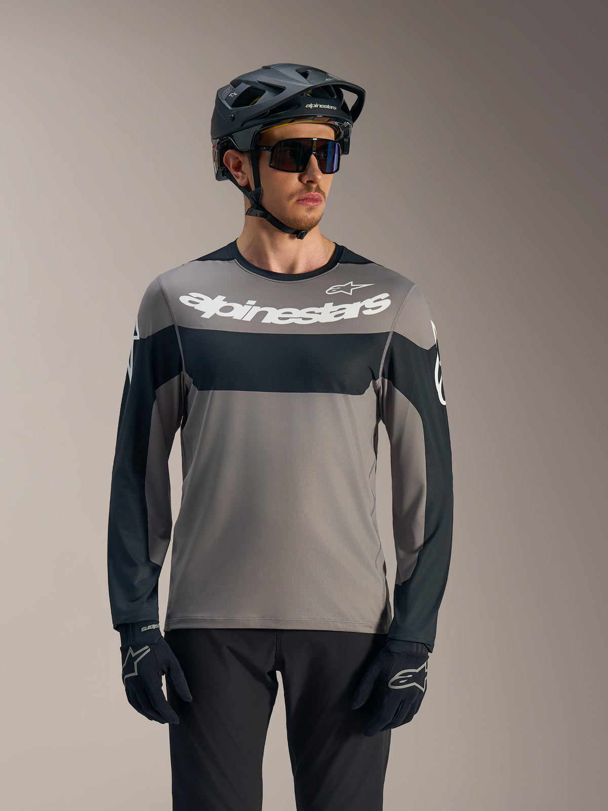 Koszulka A-Dura Race z długim rękawem, szaro-czarna z białym logo Alpinestars, stylizacja z kaskiem MTB do jazdy trailowej