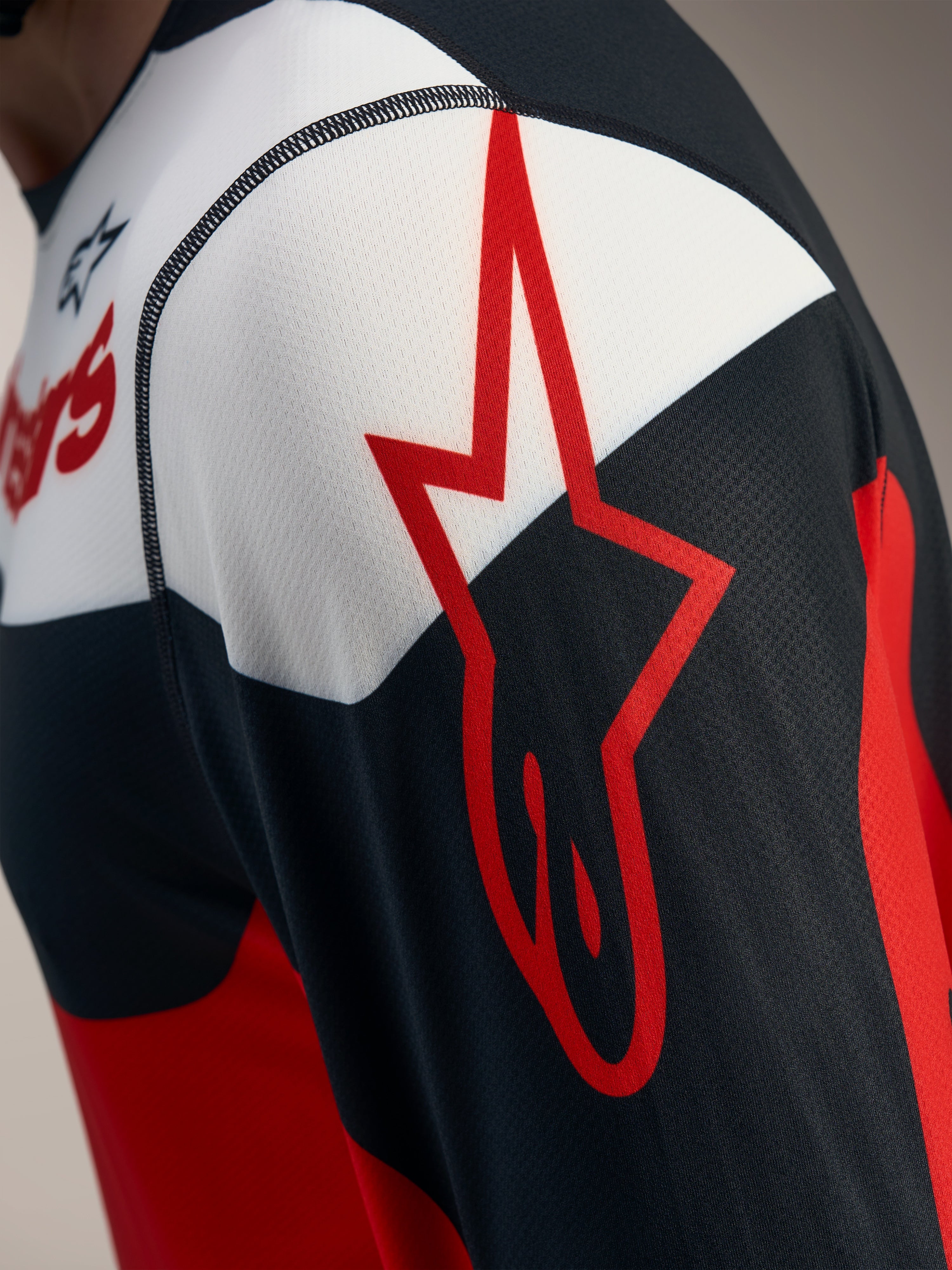 Detal czerwono-czarnej koszulki A-Dura Race z logo Alpinestars na oddychającej siateczce jacquard.
