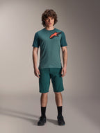 Alpinestars A-Dura Shorts w kolorze Dark Pine, męskie spodenki do kolarstwa górskiego, widoczne na modelu z dopasowaną turkusową koszulką z krótkim rękawem i czerwono-czarnym logo gwiazdy, czarne skarpetki i buty rowerowe, casualowa sportowa odzież MTB