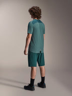 Model w spodenkach Alpinestars A-Dura w kolorze Dark Pine i pasującej zielonej koszulce Lipan z krótkim rękawem, widok z tyłu, czarne skarpety i czarne buty do kolarstwa górskiego, profesjonalna odzież MTB
