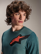 Alpinestars A-Dura Lipan Jersey, koszulka MTB z krótkim rękawem, kolor Silver Pine, z wyraźnym czerwono-czarnym logo Astars na klatce piersiowej, teksturowane żakardowe rękawy, portret z bliska modelu w profesjonalnej odzieży kolarskiej