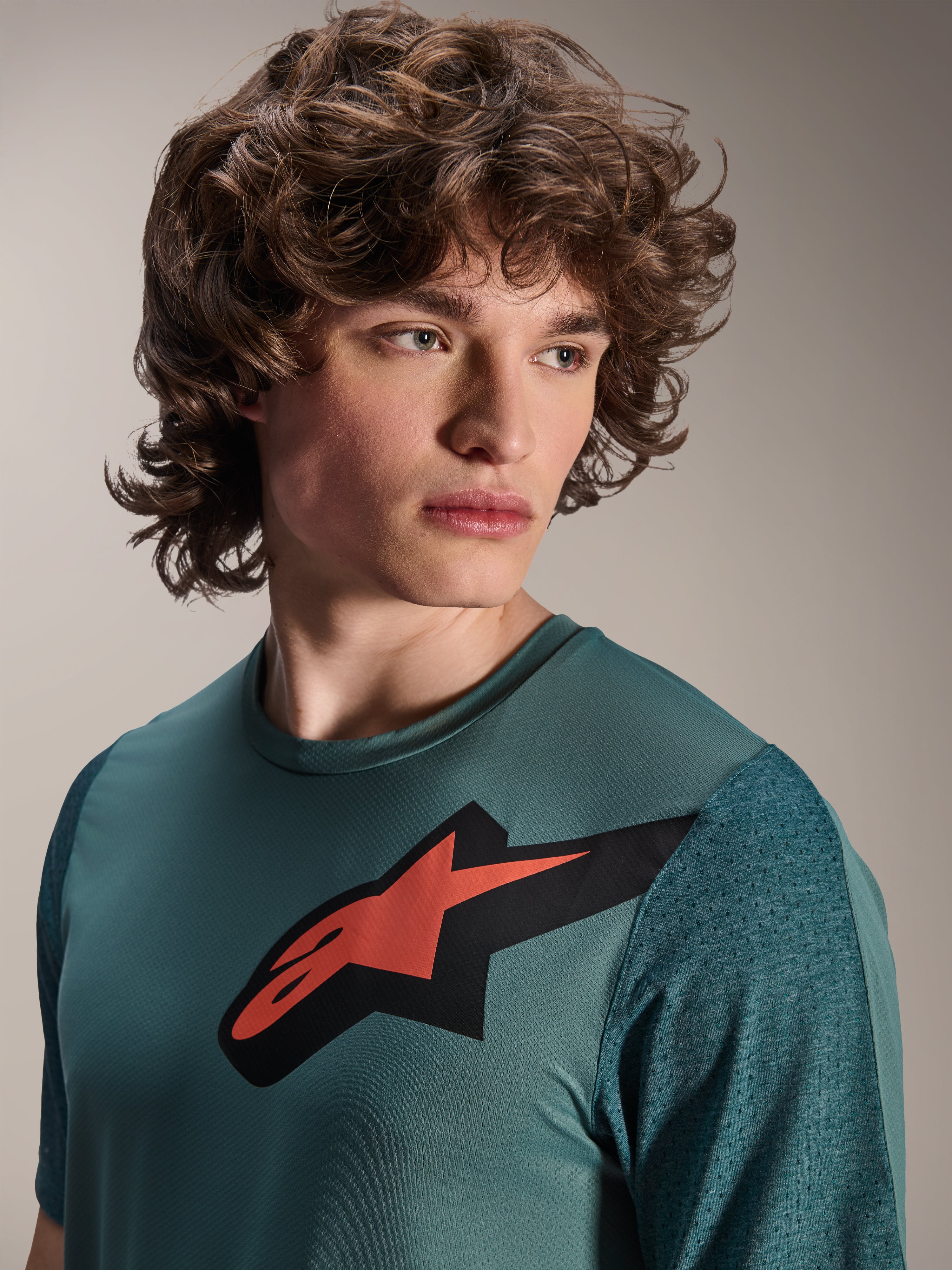 Alpinestars A-Dura Lipan Jersey, koszulka MTB z krótkim rękawem, kolor Silver Pine, z wyraźnym czerwono-czarnym logo Astars na klatce piersiowej, teksturowane żakardowe rękawy, portret z bliska modelu w profesjonalnej odzieży kolarskiej