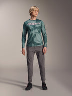 Alpinestars A-Dura Hollow Camo Long Sleeve Jersey, koszulka z długim rękawem, kolor Silver Pine Camo z zielonym wzorem moro, duże białe logo „astars” na klatce piersiowej, noszona z szarymi spodniami technicznymi i czarnymi butami rowerowymi, wysokiej jakości odzież MTB