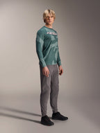Alpinestars A-Dura Hollow Camo Long Sleeve Jersey, Silver Pine Camo, koszulka z długim rękawem noszona przez modela w szarych spodniach i czarnych butach, zielony wzór kamuflażu, wyraźne białe logo ASTARS na piersi, wysokiej klasy odzież MTB