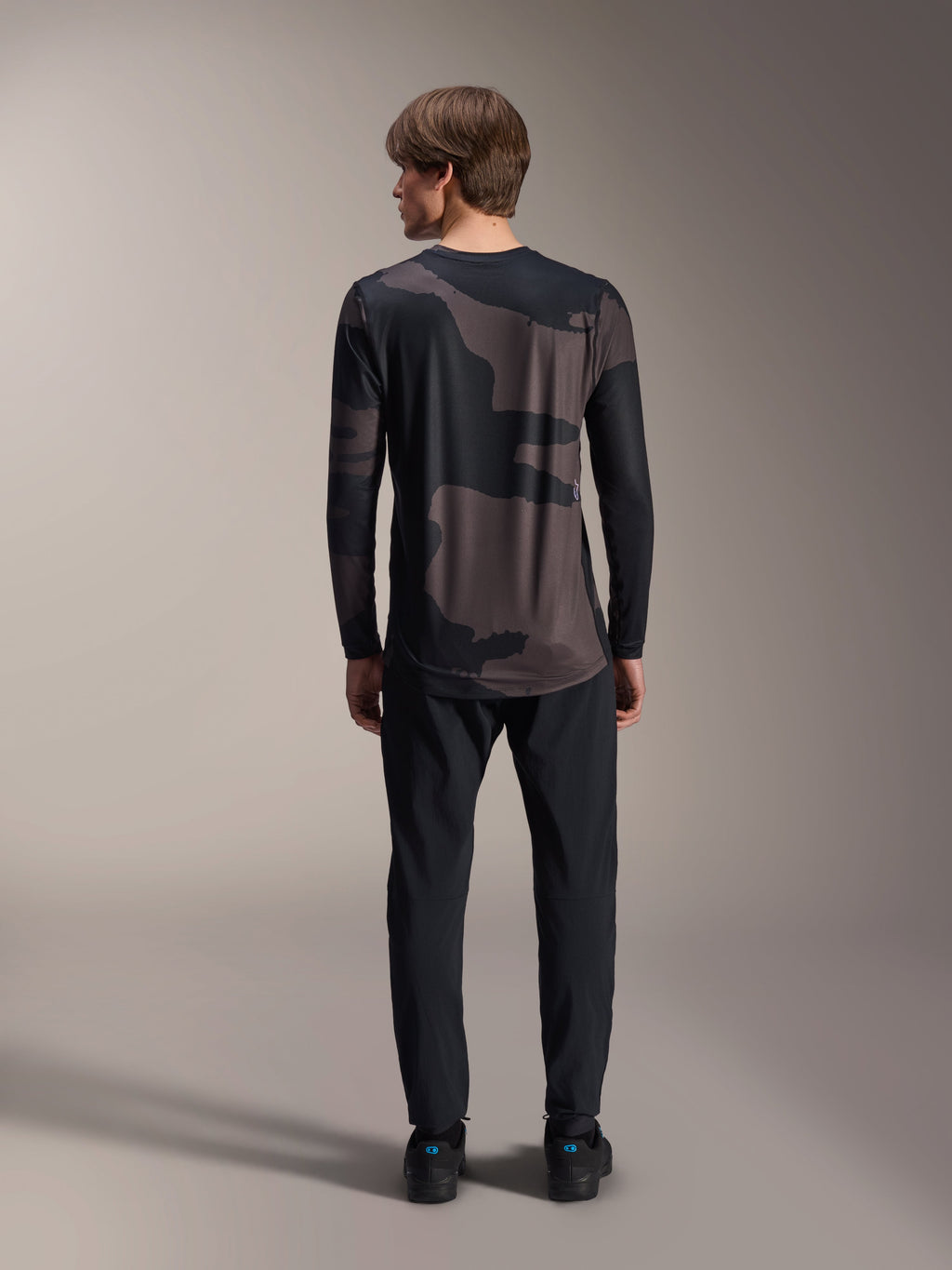 Alpinestars A-Dura Hollow Camo Long Sleeve Jersey, kolor Black Camo, widok z tyłu w czarnych spodniach, ciemny wzór kamuflażu i przedłużony tył dla lepszej osłony MTB.