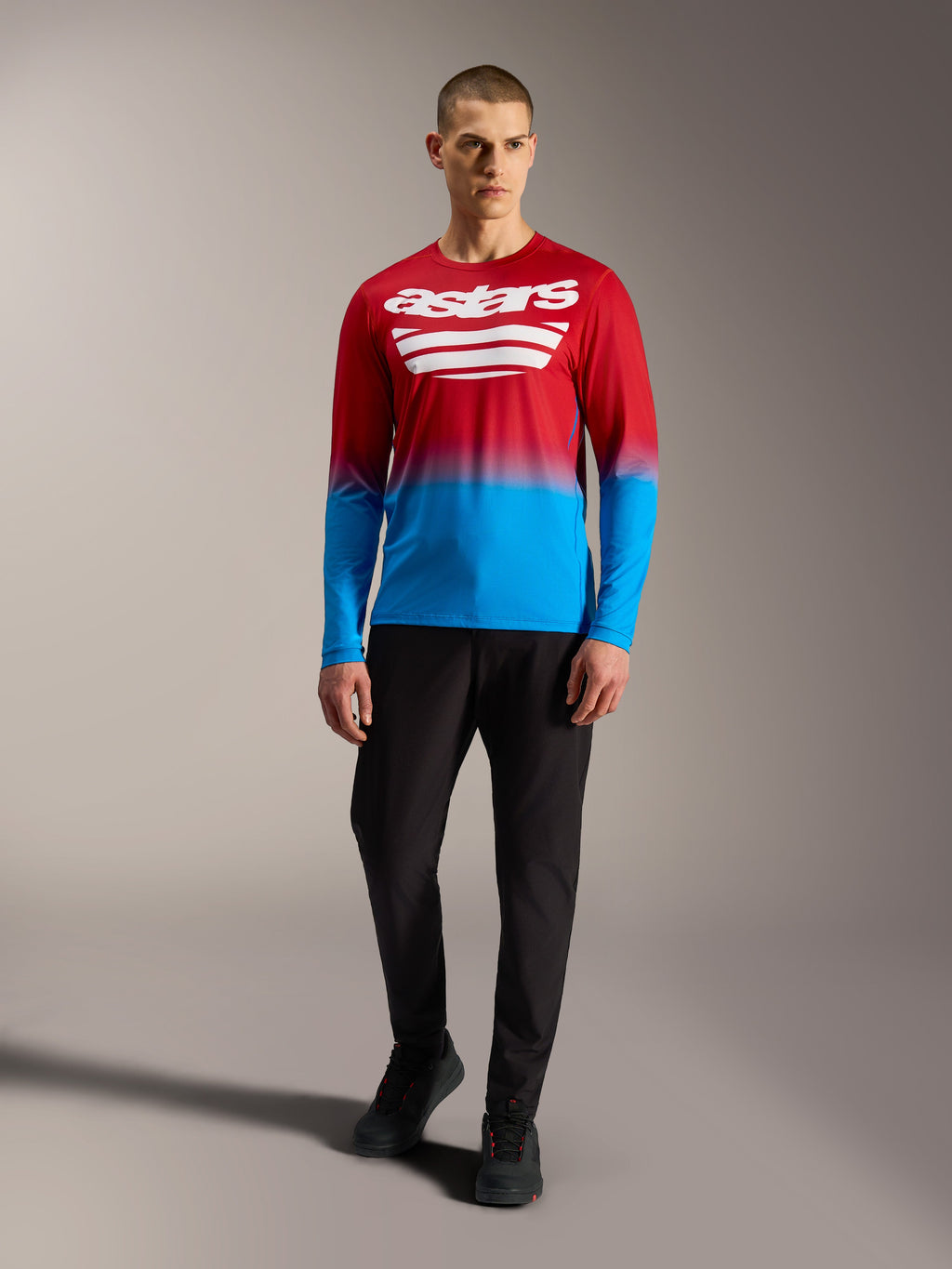 Koszulka MTB A-Dura ASTARS 2.0, czerwono-niebieski gradient, białe logo, długi rękaw, model w czarnych spodniach.