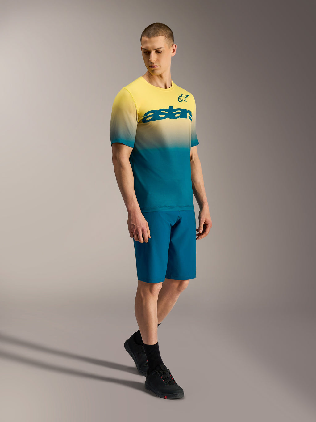 Koszulka A-Dura ASTARS 2.0 z żółto-niebieskim gradientem, krótki rękaw, logo na piersi, model w stroju MTB.
