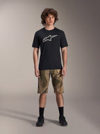 Alpinestars A-Dura Astar Short Sleeve Jersey, czarna koszulka z krótkim rękawem, duże białe logo Astars na piersi, model w szortach MTB o wzorze kamuflażu i czarnych butach rowerowych, casualowa odzież do kolarstwa górskiego.