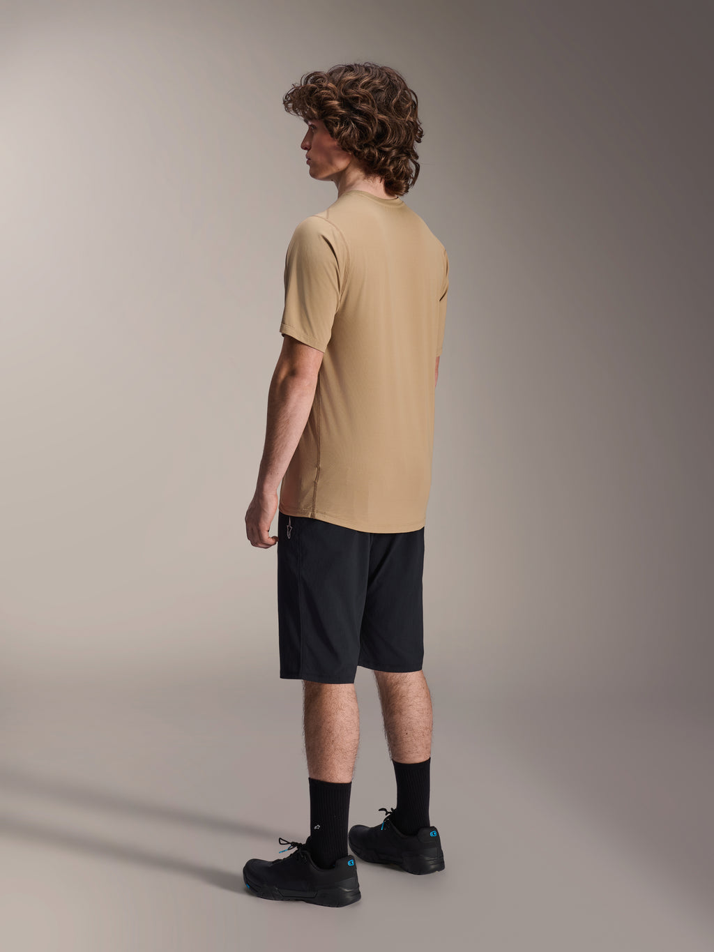 Alpinestars A-Dura Liner Shorts w kolorze czarnym i koszulka A-Dura SS w kolorze beżowym, noszone przez modela widocznego z profilu, w zestawieniu z czarnymi skarpetami i butami rowerowymi, lifestylowa odzież MTB.