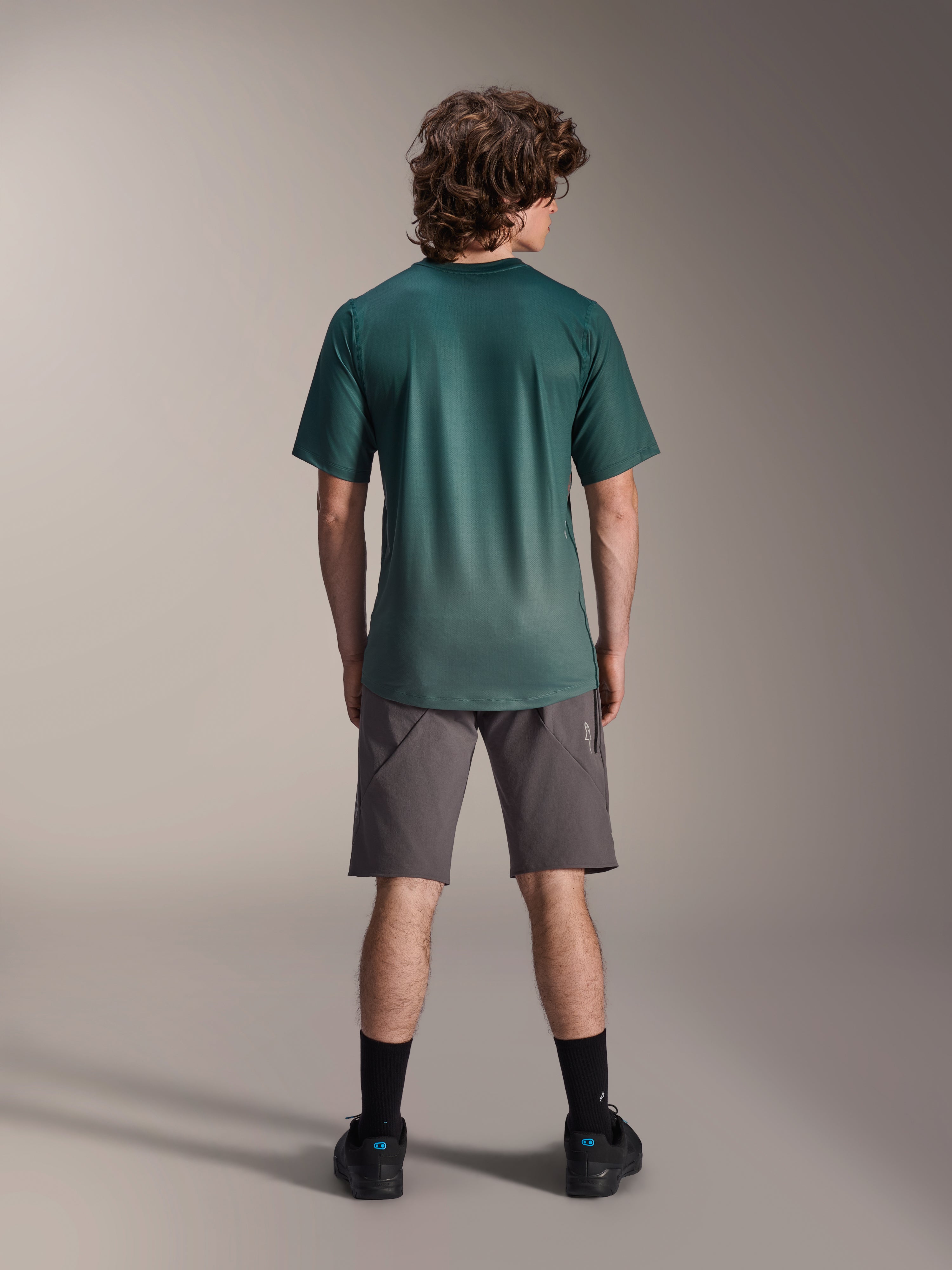 Alpinestars A-Dura Rise Jersey - krótki rękaw, kolor Silver Pine, widok od tyłu na męskiego modela w szarych szortach i czarnych skarpetach, przedłużony tył i regularny krój do jazdy na rowerze górskim