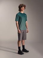 Alpinestars A-Dura Rise Jersey - Short Sleeve w kolorze Silver Pine, zielona koszulka rowerowa MTB noszona przez modela z szarymi szortami i czarnymi sneakersami, swobodny strój na szlaki MTB z małym białym logo na klatce piersiowej