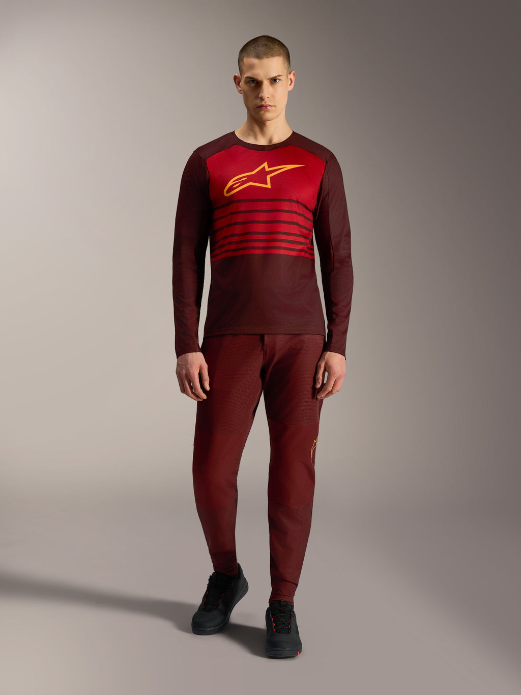 Koszulka Alpinestars A-Dura Elite 2.0 z długim rękawem, bordowa z żółtym logo i czerwonymi paskami na piersi.