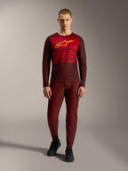 Koszulka Alpinestars A-Dura Elite 2.0 z długim rękawem, bordowa z żółtym logo i czerwonymi paskami na piersi.