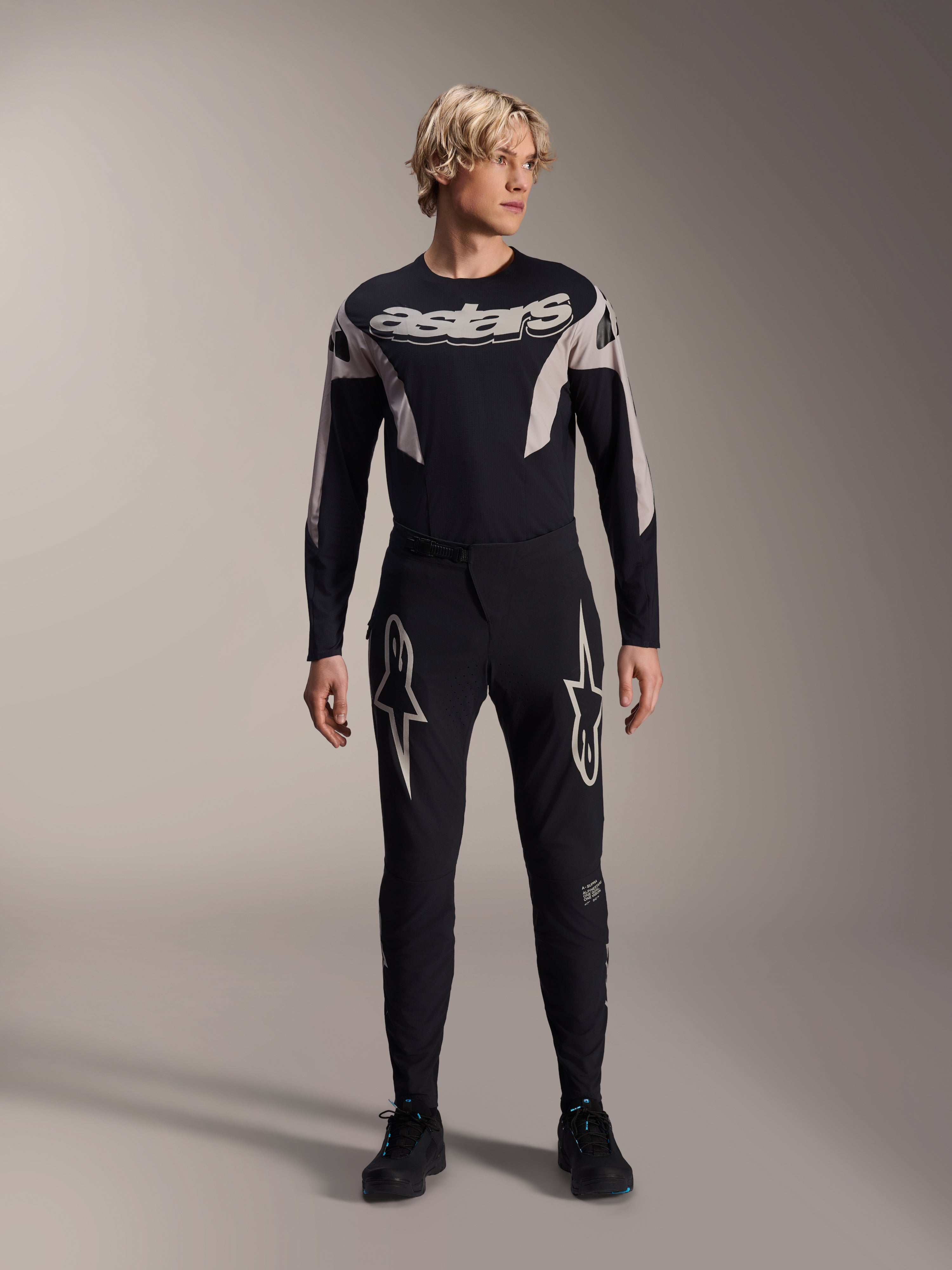 Alpinestars A-Supra Melt Jersey, koszulka MTB z długim rękawem, czarna z białym brandingiem Astars na klatce piersiowej, noszona z pasującymi czarnymi spodniami rowerowymi z logo gwiazdy, nowoczesna wyczynowa odzież kolarska