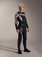 Męski model w koszulce Alpinestars A-Supra Melt Jersey - Long Sleeve, czarnej z szarymi akcentami graficznymi i logo „astars” na klatce piersiowej, w zestawie z dopasowanymi czarnymi spodniami i butami, wyczynowy zestaw MTB do wyścigów terenowych