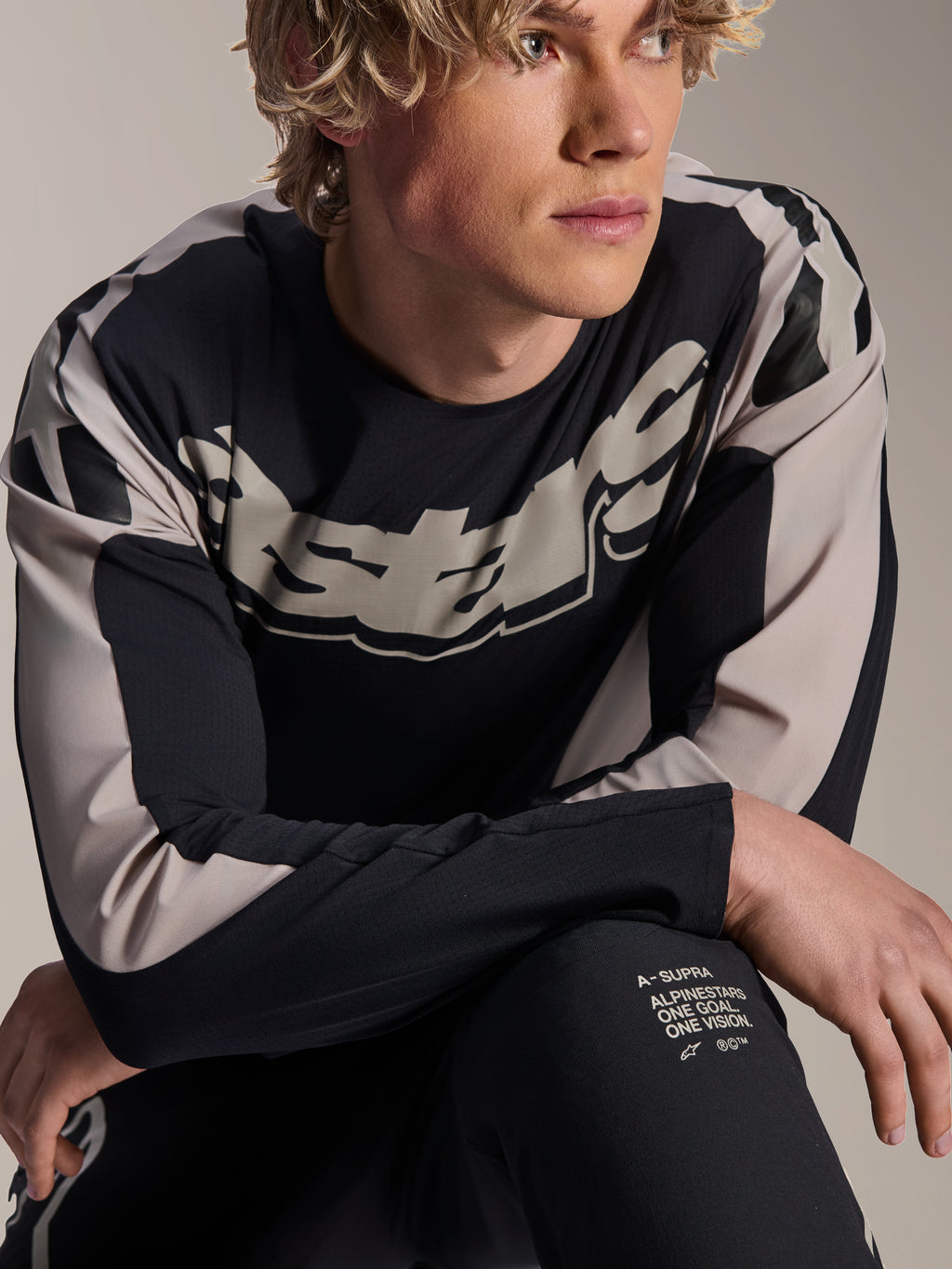 Koszulka Alpinestars A-Supra Melt, koszulka MTB z długim rękawem, czarna z jasnoszarymi grafikami, prezentowana przez modela, z wyraźnym logo na klatce piersiowej i napisem „One Goal. One Vision.”, profesjonalna odzież do kolarstwa górskiego