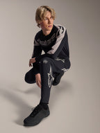 Alpinestars A-Supra Melt Pants i koszulka z długim rękawem, czarno-szare, z wyraźnym białym brandingiem i logo gwiazdy, model w pozycji kucającej, dopasowany zestaw wyścigowy MTB