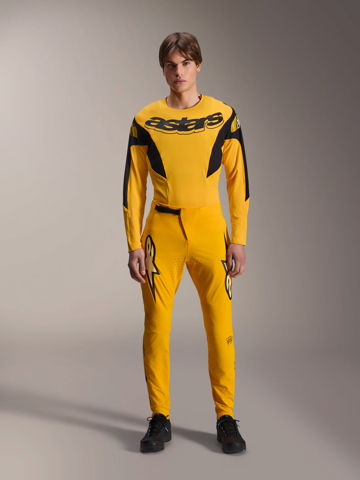 Zestaw odzieży Alpinestars Limited Edition A-Supra Melt Gold, profesjonalny komplet MTB, ciemnożółty i czarny, model w koszulce z długim rękawem z wyraźnym logo „astars” na piersi i pasujących spodniach, laserowo wycinana wentylacja na udach, zapięcie zapadkowe w pasie