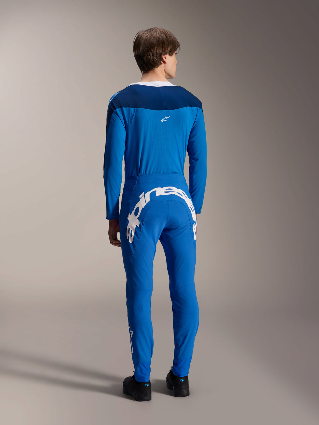 Spodnie Alpinestars A-Supra Melt i pasująca koszulka z długim rękawem, niebieskie, widok od tyłu podkreślający duży biały napis Alpinestars na tylnym karczku, wydajna odzież MTB o elastycznym, sportowym kroju