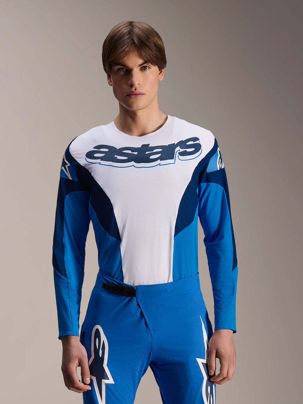 Alpinestars A-Supra Melt Jersey z długim rękawem, niebiesko-biała koszulka MTB, z wyraźnym brandingiem astars na klatce piersiowej, ciemnoniebieskie rękawy, noszona z pasującymi niebieskimi spodniami wyścigowymi z białym logo gwiazdy, profesjonalna odzież do kolarstwa górskiego