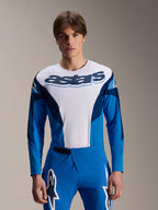 Alpinestars A-Supra Melt Jersey z długim rękawem, niebiesko-biała koszulka MTB, z wyraźnym brandingiem astars na klatce piersiowej, ciemnoniebieskie rękawy, noszona z pasującymi niebieskimi spodniami wyścigowymi z białym logo gwiazdy, profesjonalna odzież do kolarstwa górskiego