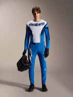 Rowerzysta w koszulce Alpinestars A-Supra Melt Jersey z długim rękawem w kolorze niebiesko-białym, z logo „astars” na klatce piersiowej, pasujące niebieskie spodnie, czarne rękawiczki, trzymający czarny kask, wyczynowy zestaw wyścigowy MTB.