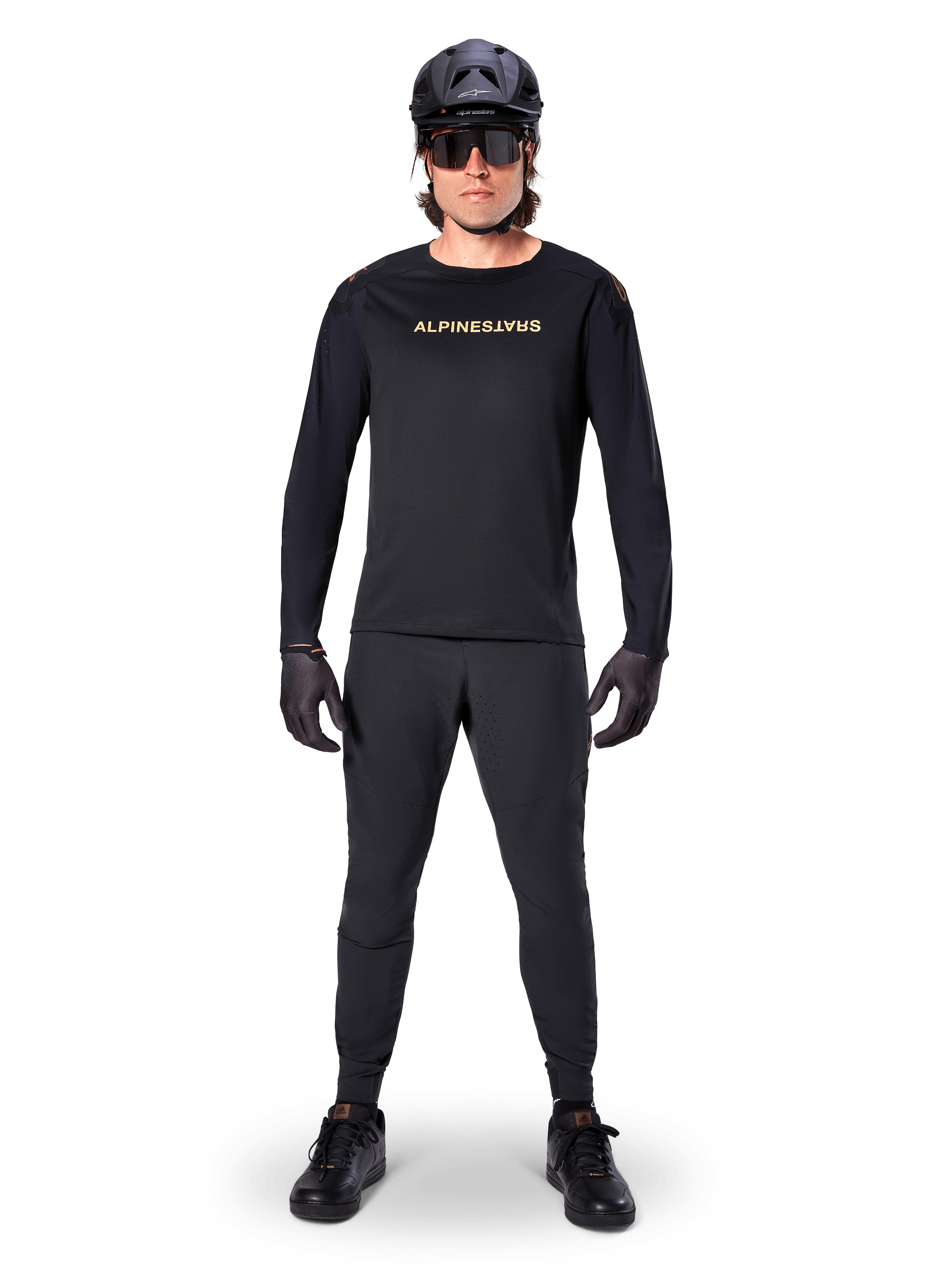 Alpinestars A-Aria Polartec Switch Long Sleeve Jersey, czarna, prezentowana przez kolarza w komplecie z czarnymi spodniami technicznymi, czarnym kaskiem, okularami przeciwsłonecznymi i czarnymi rękawicami, profesjonalny strój MTB na terenowe szlaki