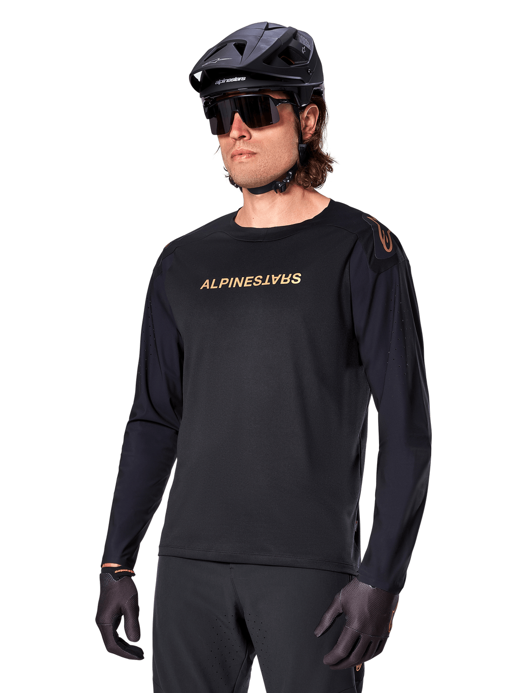 Alpinestars A-Aria Polartec Switch Long Sleeve Jersey, czarna ze złotym logo, odzież do jazdy na rowerze górskim MTB, noszona z czarnym kaskiem i okularami przeciwsłonecznymi, laserowo wycinana wentylacja na rękawach oraz odprowadzający wilgoć materiał Polartec zapewniający wydajność w terenie
