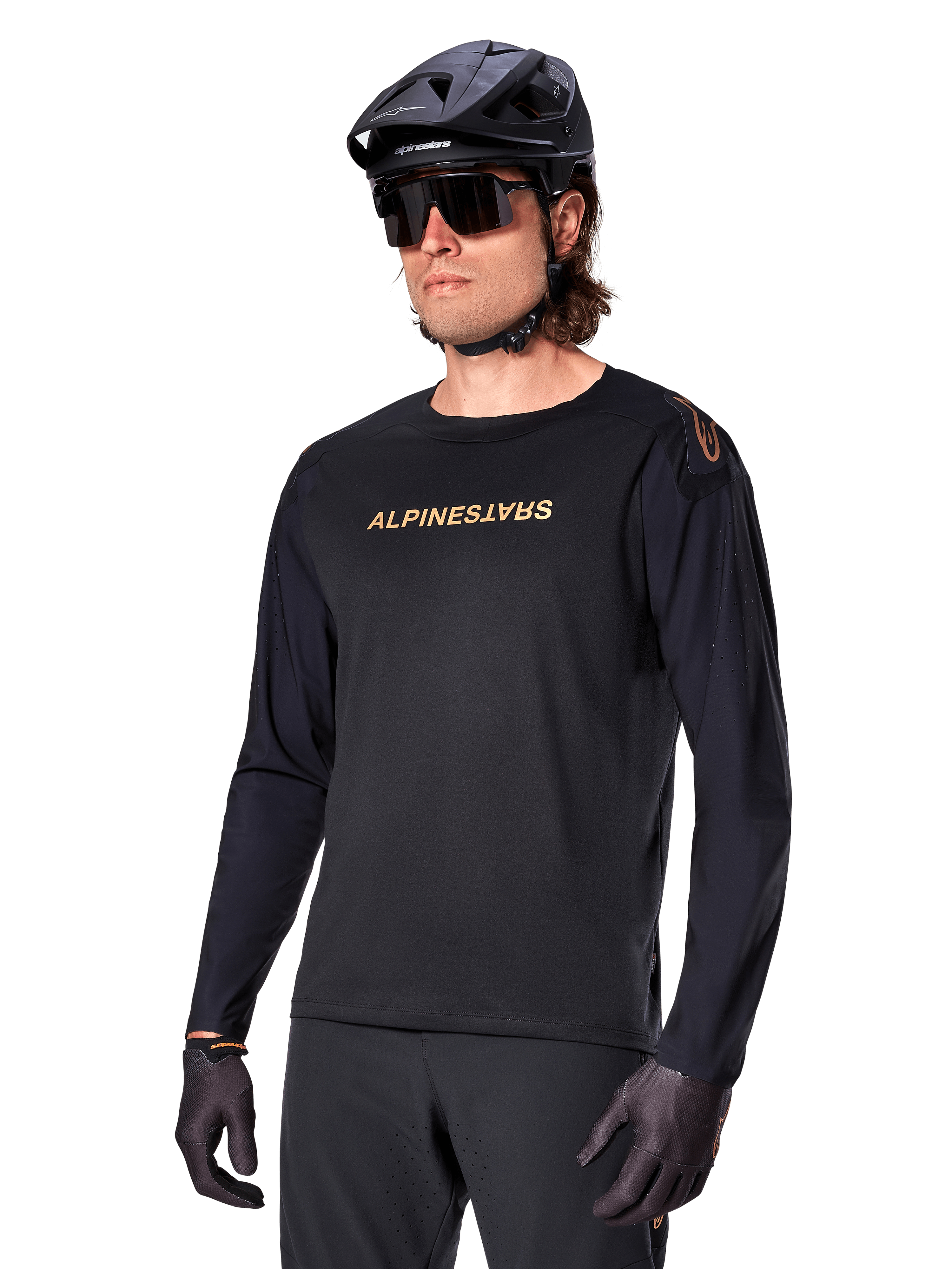 Alpinestars A-Aria Polartec Switch Long Sleeve Jersey, czarna ze złotym logo, odzież do jazdy na rowerze górskim MTB, noszona z czarnym kaskiem i okularami przeciwsłonecznymi, laserowo wycinana wentylacja na rękawach oraz odprowadzający wilgoć materiał Polartec zapewniający wydajność w terenie