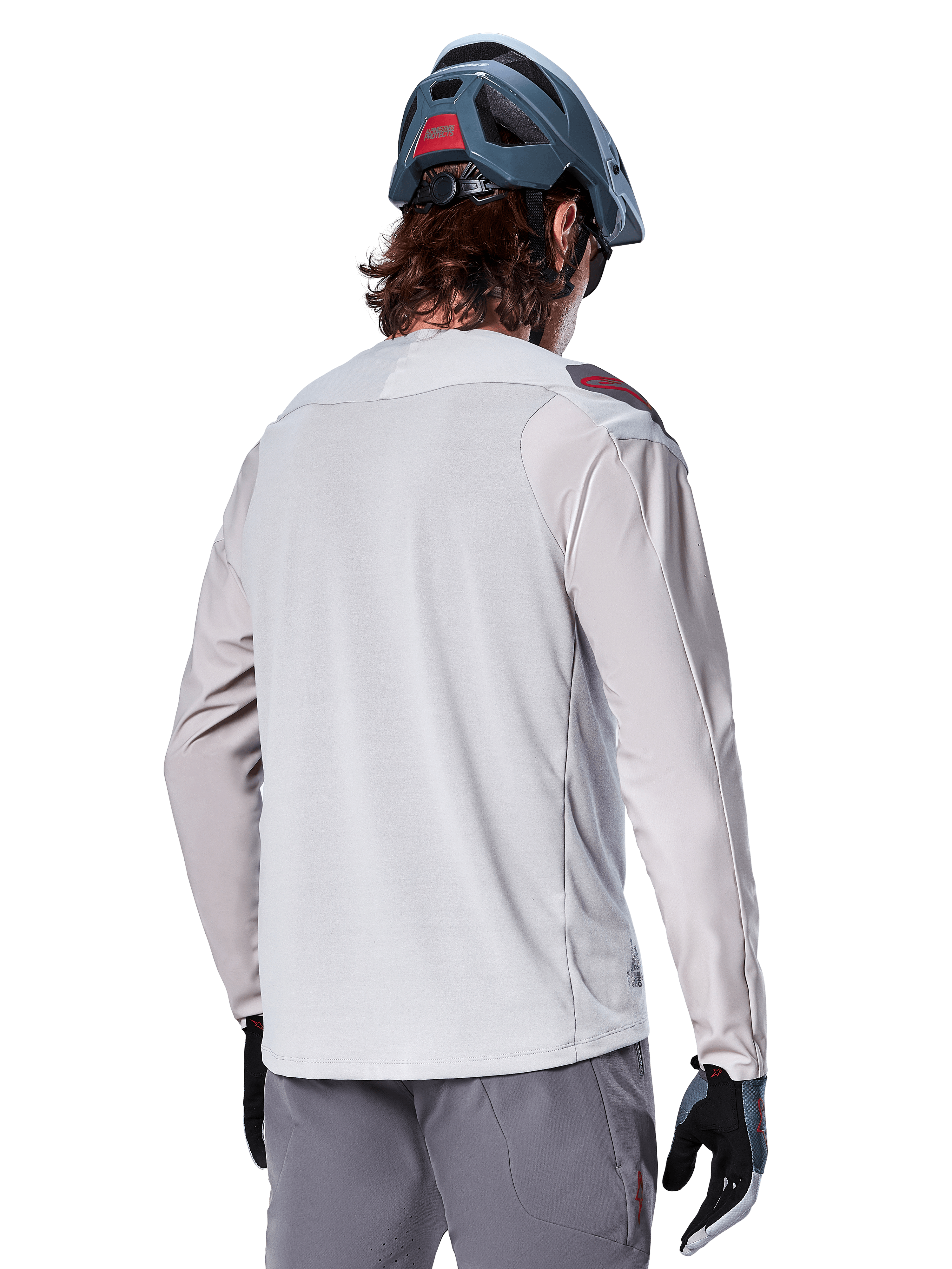 Alpinestars A-Aria Polartec Switch Long Sleeve Jersey, jasnoszara, widok z tyłu na rowerzyście, w zestawieniu z niebieskim kaskiem MTB i szarymi spodniami, techniczna odzież do kolarstwa górskiego na szlaki terenowe