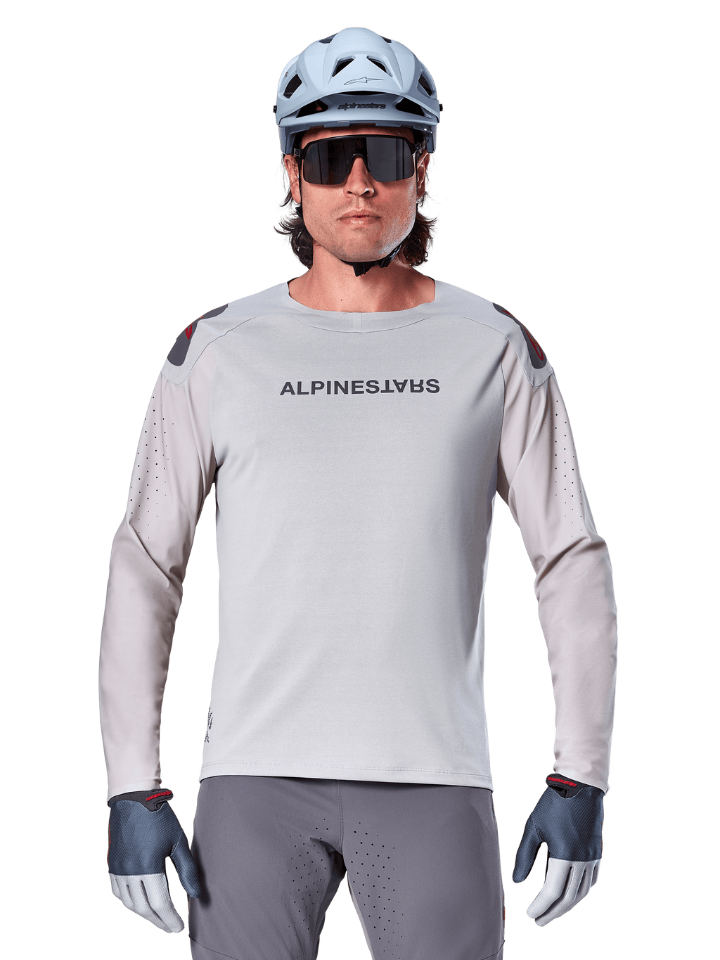 Alpinestars A-Aria Polartec Switch Long Sleeve Jersey, jasnoszara koszulka rowerowa MTB z laserowymi perforacjami na rękawach i logo na klatce piersiowej, noszona z jasnoniebieskim kaskiem, okularami przeciwsłonecznymi i szarymi rękawiczkami