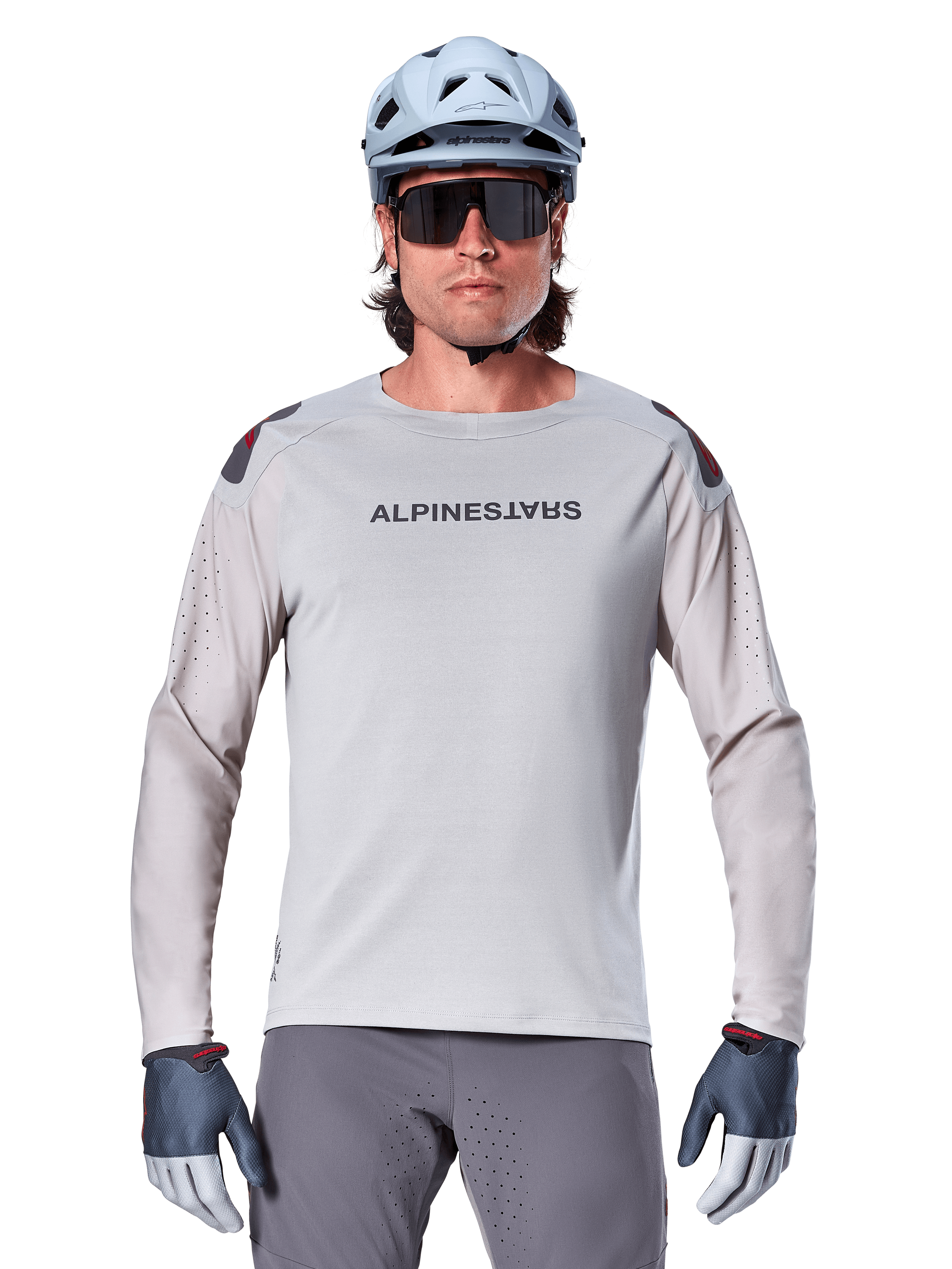 Alpinestars A-Aria Polartec Switch Long Sleeve Jersey, jasnoszara koszulka rowerowa MTB z laserowymi perforacjami na rękawach i logo na klatce piersiowej, noszona z jasnoniebieskim kaskiem, okularami przeciwsłonecznymi i szarymi rękawiczkami
