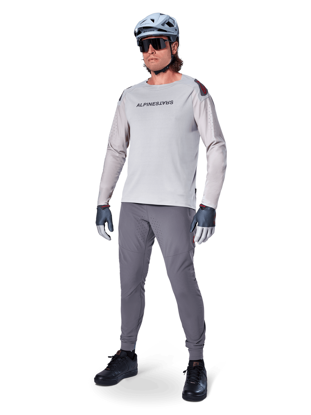 Alpinestars A-Aria Polartec Switch Jersey, koszulka MTB z długim rękawem, jasnoszara, zestawiona z ciemnoszarymi spodniami rowerowymi, kaskiem i rękawicami, laserowo perforowane rękawy i logo Alpinestars na klatce piersiowej.