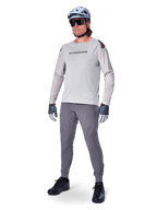 Alpinestars A-Aria Polartec Switch Jersey, koszulka MTB z długim rękawem, jasnoszara, zestawiona z ciemnoszarymi spodniami rowerowymi, kaskiem i rękawicami, laserowo perforowane rękawy i logo Alpinestars na klatce piersiowej.