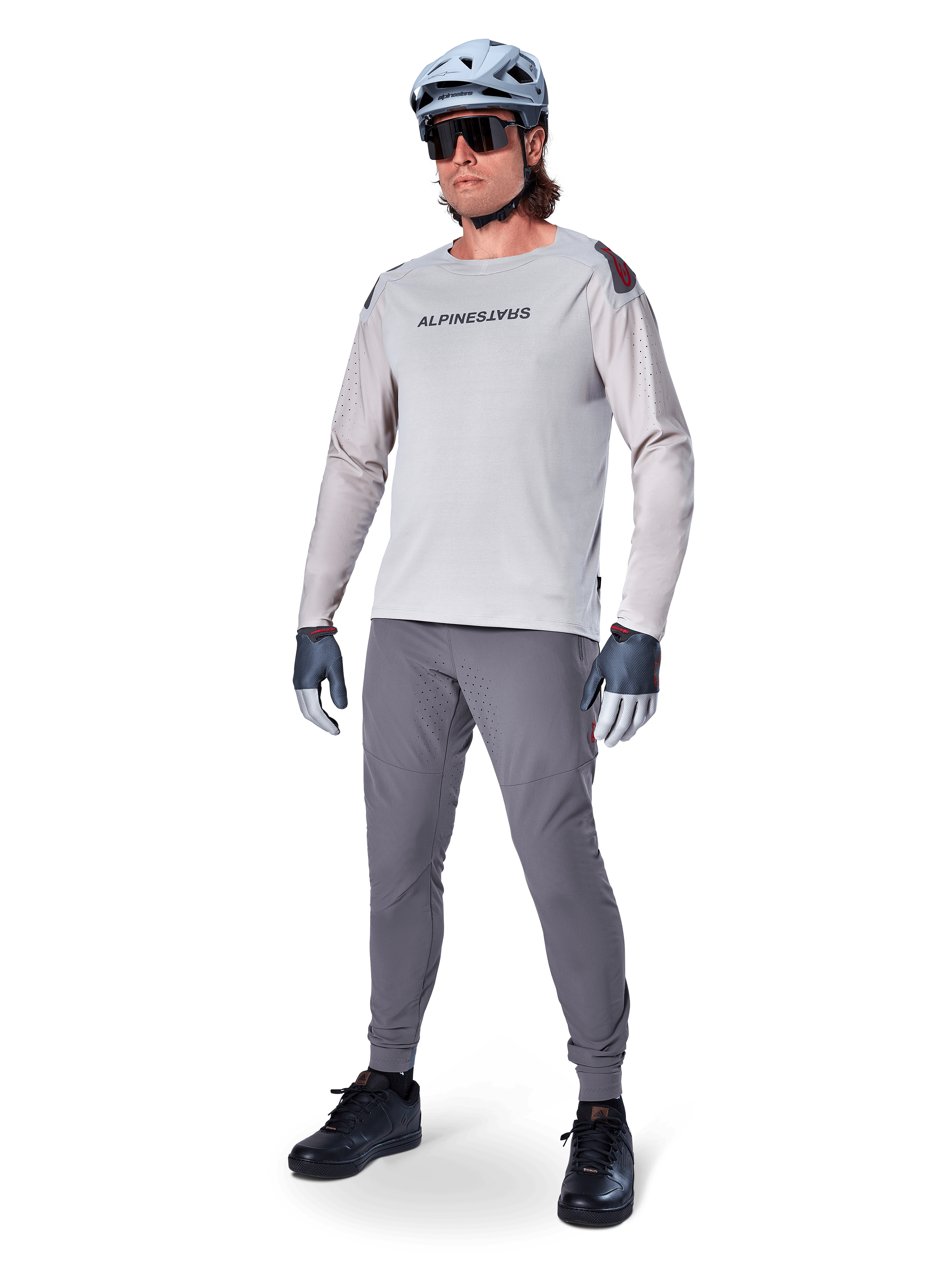 Alpinestars A-Aria Polartec Switch Jersey, koszulka MTB z długim rękawem, jasnoszara, zestawiona z ciemnoszarymi spodniami rowerowymi, kaskiem i rękawicami, laserowo perforowane rękawy i logo Alpinestars na klatce piersiowej.